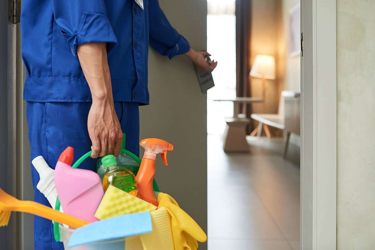 A cleaner walking into a hotel room with cleaning supplies and equipment.